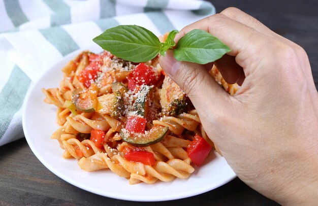 Ręczne układanie liści bazylii na półmisku ze świeżo ugotowanego makaronu fusilli pełnoziarnistego w sosie pomidorowym