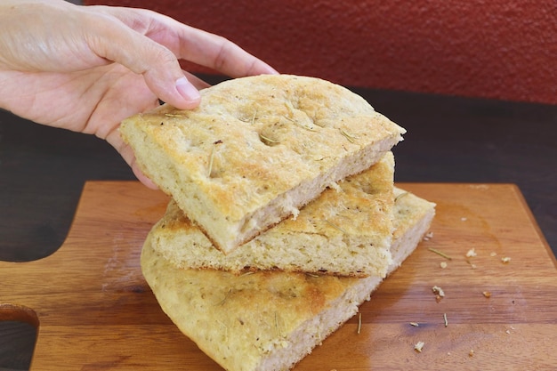 Ręczne zbieranie kromki smacznego chleba Focaccia z rozmarynem ułożone na drewnianej desce do krojenia chleba