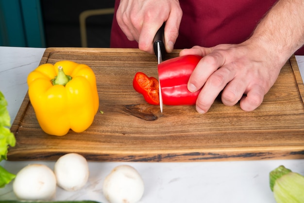 Ręcznie krojony pieprz z ceramicznym nożem. Warzywa coraz krojone na drewnianej desce do krojenia. Przygotowanie żywności i przepisy kulinarne. Menu wegetariańskie i zdrowa dieta. Koncepcja produktów ekologicznych.