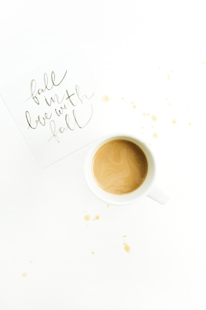 Ręcznie napisany cytat "Zakochaj się w upadku" i filiżanka kawy na białej powierzchni