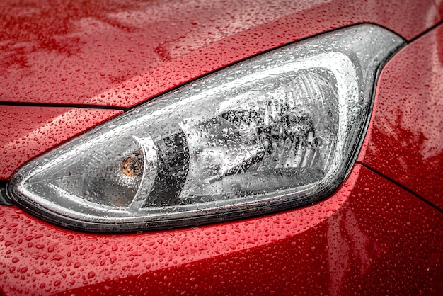 Reflektor czerwonego samochodu w kroplach deszczu. Krople deszczu. Czerwony samochód. Reflektor samochodowy. Zła pogoda.