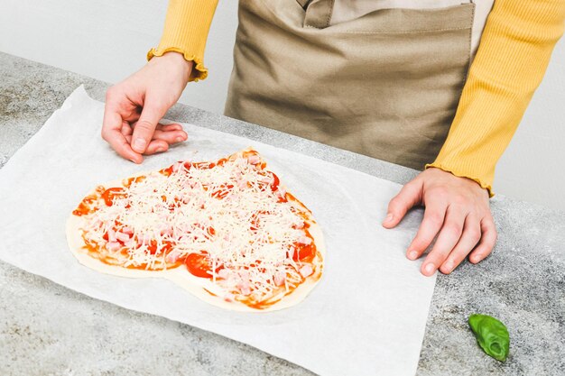 Ręka białej nastolatki nalewającej ser na pizza na Walentynki.