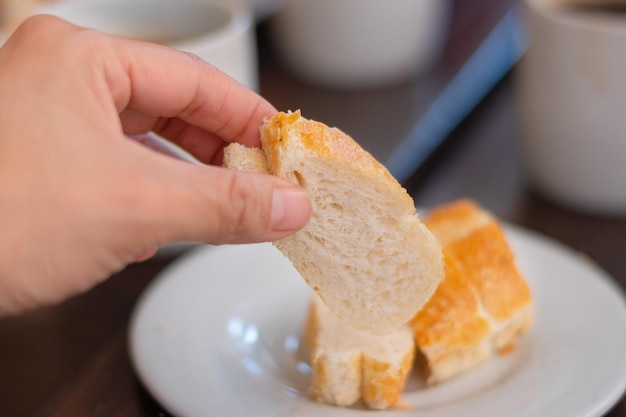 Ręka biorąca kawałek chleba w restauracji na śniadanie na białym talerzu