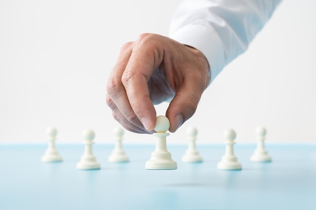 Ręka biznesmena ustawiająca figurę szachową pionka przed xApozostałe pionki na niebieskim biurku w obrazie koncepcyjnym