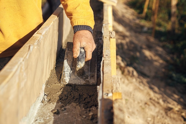 Ręka budowniczego z kielnią pracującą z betonem w szalunkach drewnianych Plac budowy