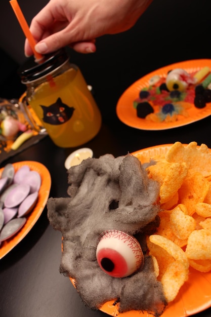 Zdjęcie ręka chwyta słomkę z dzbana lub słoika z pomarańczową sodą przerażające słodycze i cukierki impreza halloween