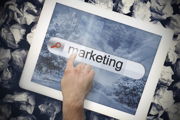 Zdjęcie ręka dotyka słowa marketing na pasku wyszukiwania na ekranie tabletu na zmiętych papierach