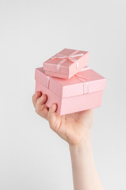 Ręka dziecka trzymająca dwa pudełka na prezenty z różową kokardą białym i szarym tłem z miejscem na kopię