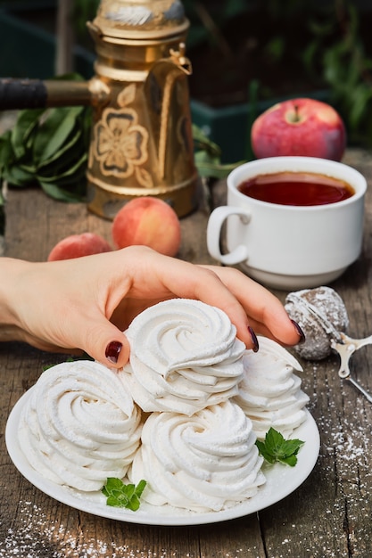 Ręka Dziewczyny Bierze Zefir (marshmallow) Z Białego Talerza, Filiżanki Herbaty I Owoców Na Vintage Stole, Zbliżenie, Podwieczorek W Ogrodzie. Zwiewne Rosyjskie Słodycze