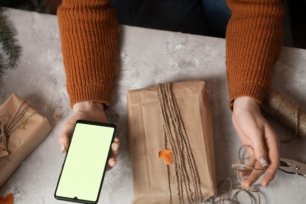 Zdjęcie ręka dziewczyny trzyma telefon obok stołu są prezenty pakowanie prezentów zamów pakowanie prezentów