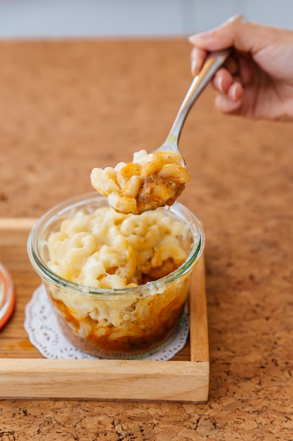 Ręka jest zgarnięcie Macaroni Cheese Pieczony z sosem mięsnym w szklanej misce.