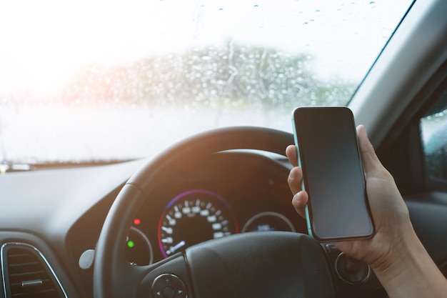 Ręka kobiety na kierownicy jazdy samochodem przy użyciu smartfona światło słoneczne tło.