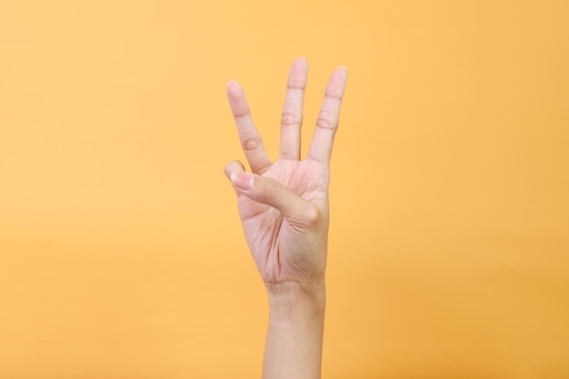 Ręka kobiety pokazująca znak numer trzy na żółtym tle