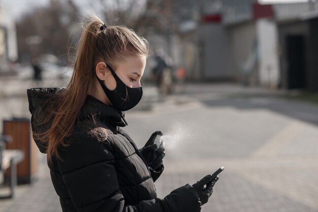 Ręka kobiety rozpyla alkohol, spray dezynfekujący na telefon komórkowy, zapobiega infekcji wirusem Covid-19, zanieczyszczeniu zarazkami lub bakteriami, wyciera telefon lub czyści telefon w celu wyeliminowania, wybuchu koronawirusa