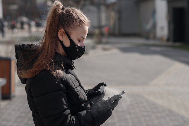 Ręka kobiety rozpyla alkohol, spray dezynfekujący na telefon komórkowy, zapobiega infekcji wirusem Covid-19, zanieczyszczeniu zarazkami lub bakteriami, wyciera telefon lub czyści telefon w celu wyeliminowania, wybuchu koronawirusa