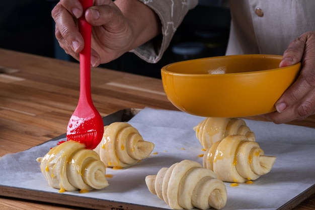 Ręka kobiety szczotkuje pokonane jajka na croissantach, by umieścić je w piekarniku.