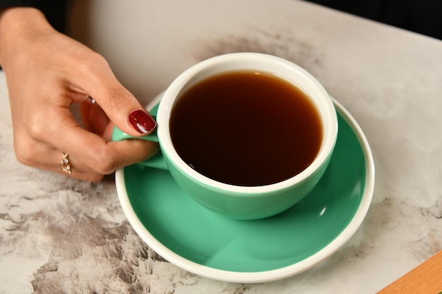 Ręka kobiety trzyma filiżankę herbaty i zieloną filiżankę herbaty.