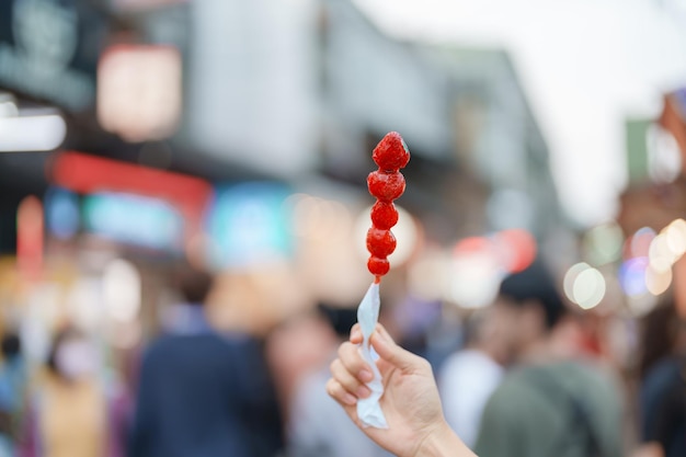 Ręka kobiety trzymającej szpikulec truskawkowy powlekany karmelem na nocnym targu Koncepcja jedzenia ulicznego i podróży