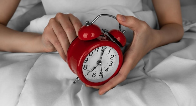 Ręka kobiety Uruchamia czerwony budzik w jej łóżku