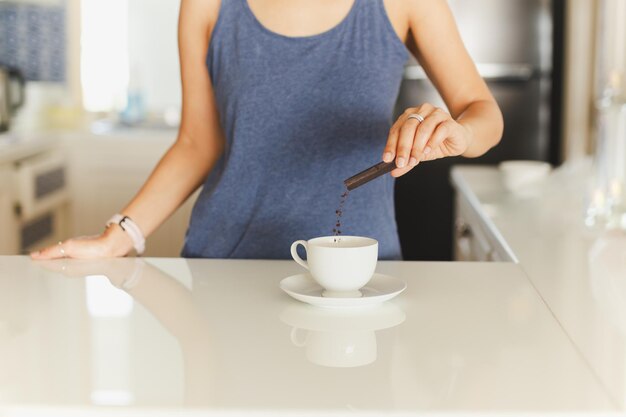 Ręka kobiety wlewa saszetkę z kawą rozpuszczalną do filiżanki