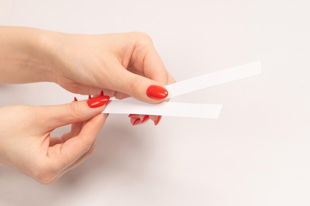 Ręka kobiety z czerwonymi paznokciami z paskami testowymi do perfum na białym tle