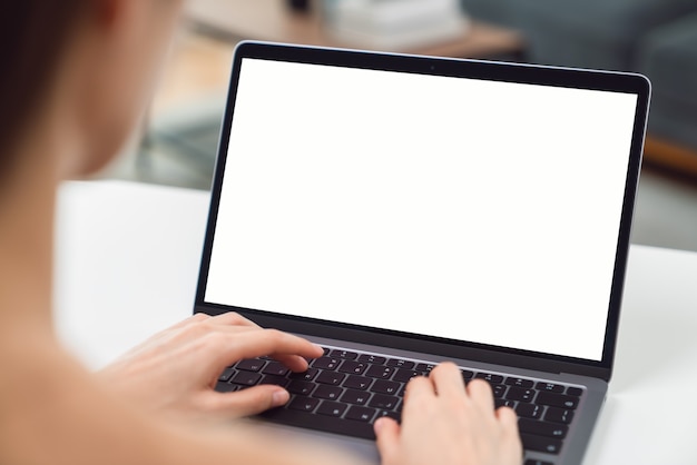 Ręka kobiety za pomocą laptopa i siedząc na stole w domu, makieta pustego ekranu aplikacji.