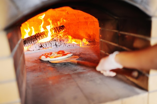 Ręka kucharza lub piekarza z apetyczną pizzą na tle gorącego pieca.