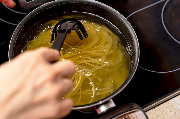 Ręka kucharza miesza łyżką cedzakową spaghetti gotowane w rondlu