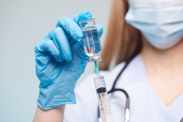 Ręka lekarza nosi rękawiczkę medyczną trzymającą strzykawkę podczas przyjmowania płynnej szczepionki