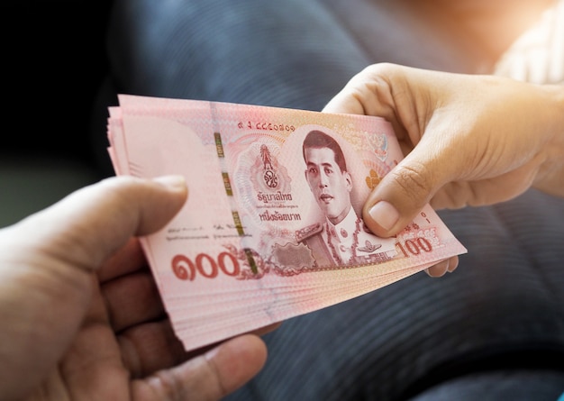 ręka ludzi przekazuje pieniądze tajskiego bahta z Tajlandii na rękę, która czeka na odbiór.