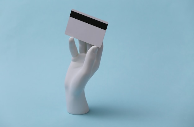 Ręka manekina białego trzyma kartę bankową na niebieskim tle. Zakupy, kredyt, pieniądze online