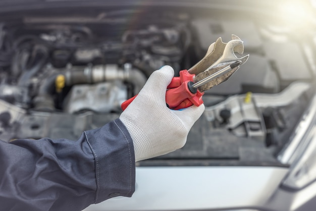 Ręka mechanika ze śrubokrętem do naprawy lub sprawdzenia samochodu w garażu. serwis samochodowy