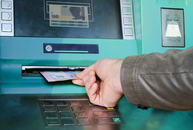 Ręka mężczyzny bierze pieniądze z bankomatu.
