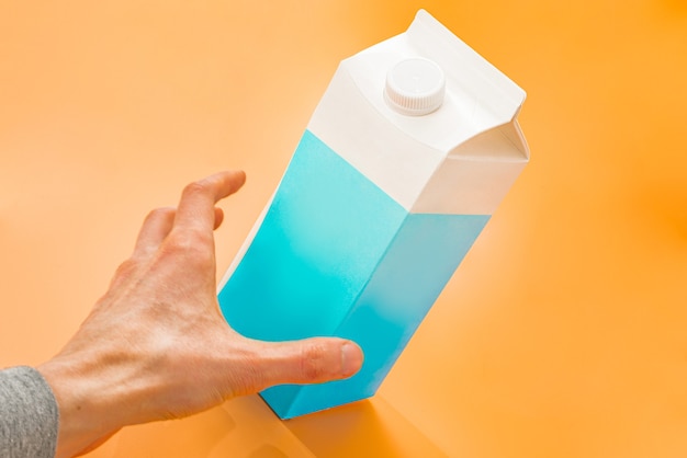 Ręka Mężczyzny Chwytająca Niebiesko-białą Papierową Torebkę Mleka Na Pomarańczowym Tle Duża Pojemność Grab