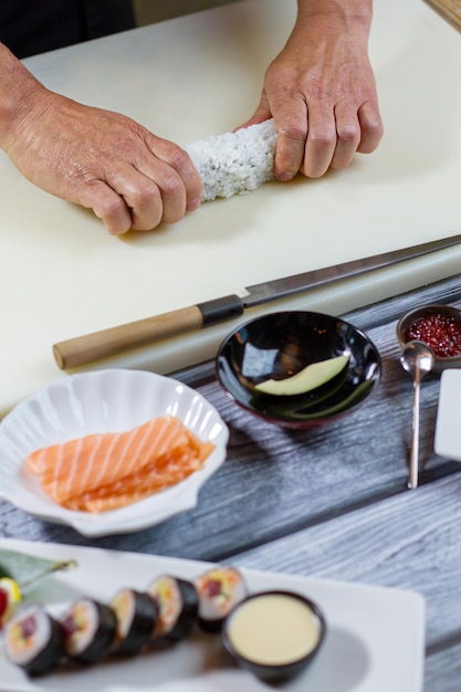 Zdjęcie ręka mężczyzny dotyka rolki sushi. nóż obok kawałka awokado. szef kuchni demonstruje nowy przepis. sekrety kuchni japońskiej.