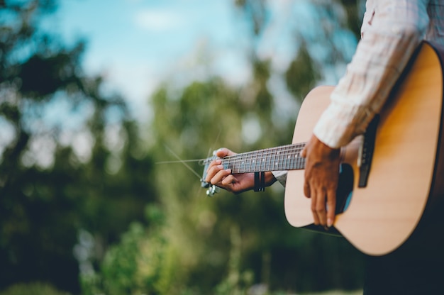 Ręka mężczyzny gra na gitarze akustycznej, gra na gitarze w ogrodzie