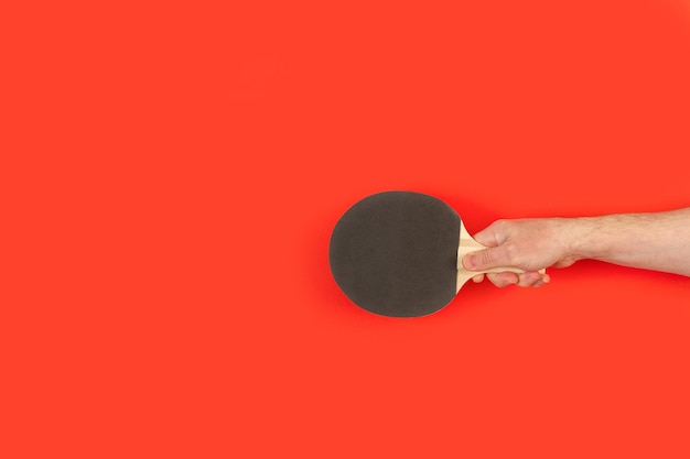 Zdjęcie ręka mężczyzny trzyma czarne wiosło do ping ponga na czerwonym tle z miejsca na kopię