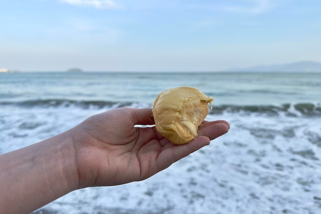 Ręka mężczyzny trzyma kawałek nieprzyjemnie pachnącego dojrzałego duriana na tle wody morskiej oceanu w tropikalnym kraju