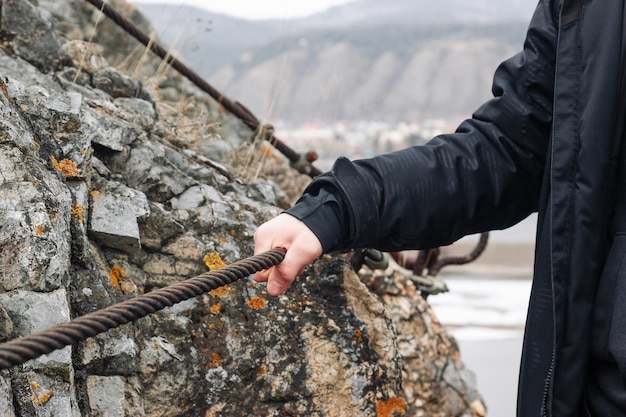 Ręka mężczyzny trzyma się metalowego kabla na tle skały