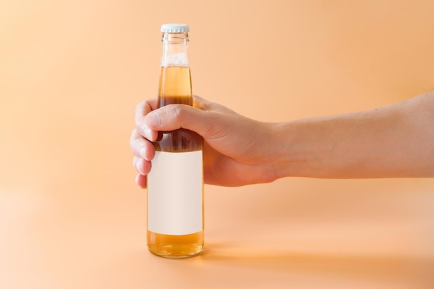 Ręka mężczyzny trzyma szklaną butelkę piwa z białą pustą etykietą na pomarańczowym tle Cool Golden Drunk Fluid Gold Warzony alkoholowy orzeźwiający pub Chill Addicted Addict Drinker