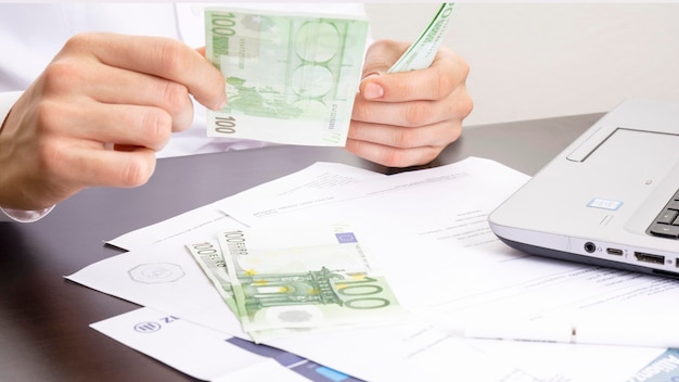 Ręka mężczyzny wyciąga banknoty o wartości stu euro na tle biurowego stołu z komputerem