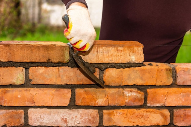 Ręka mężczyzny z pacą budowlaną usuwa nadmiar zaprawy cementowej z muru podczas wznoszenia muru