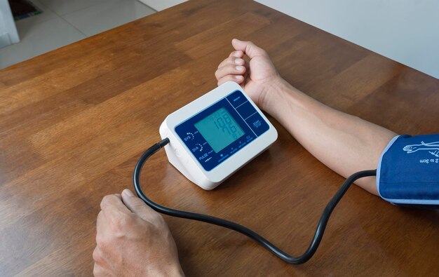 Ręka mężczyzny za pomocą cyfrowego ciśnieniomierza do pomiaru ciśnienia krwi na drewnianym stole