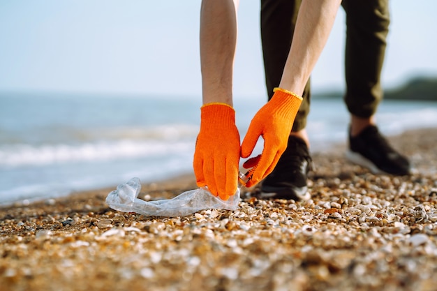Ręka mężczyzny zbiera plastikową butelkę na plaży. Wolontariusz w rękawicach ochronnych zbiera plastik butelki.