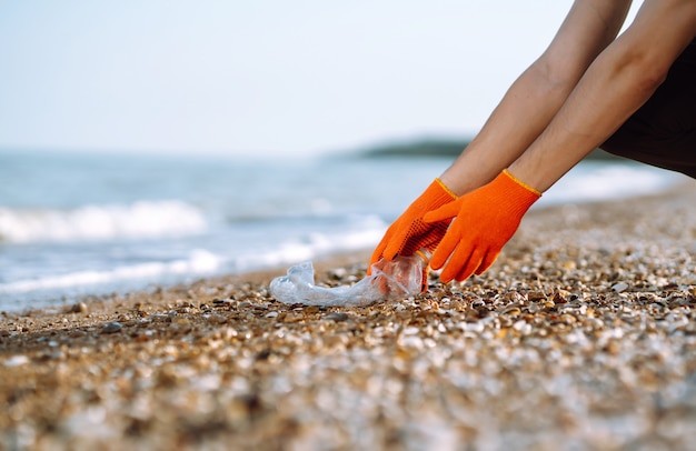 Ręka mężczyzny zbiera plastikową butelkę na plaży. Wolontariusz w rękawicach ochronnych zbiera plastik butelki.