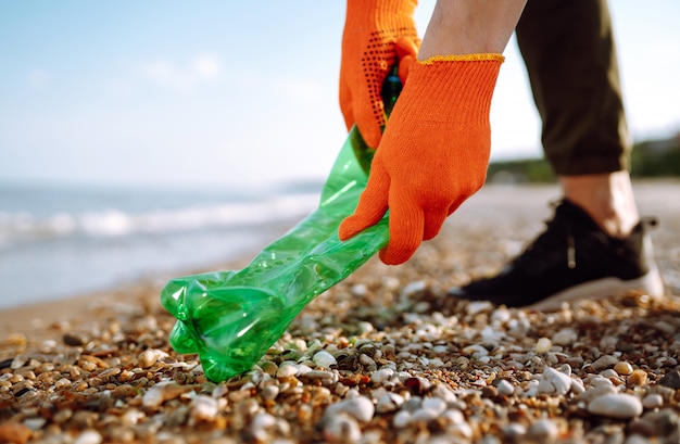 Ręka mężczyzny zbiera plastikową butelkę na plaży.