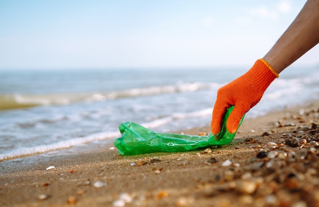 Ręka mężczyzny zbiera plastikową butelkę na plaży.