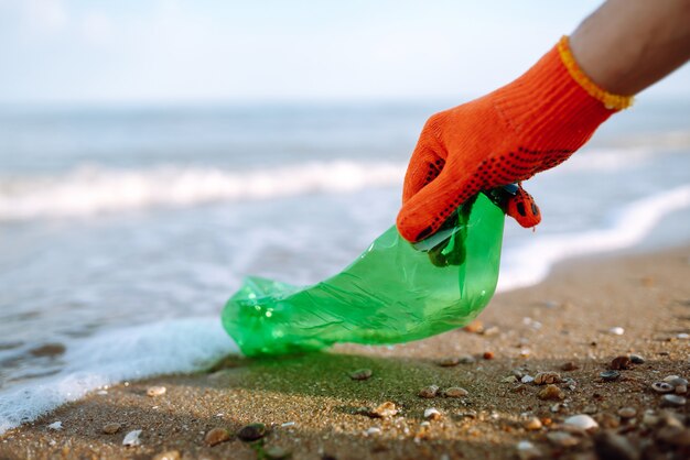 Ręka mężczyzny zbiera plastikową butelkę na plaży.