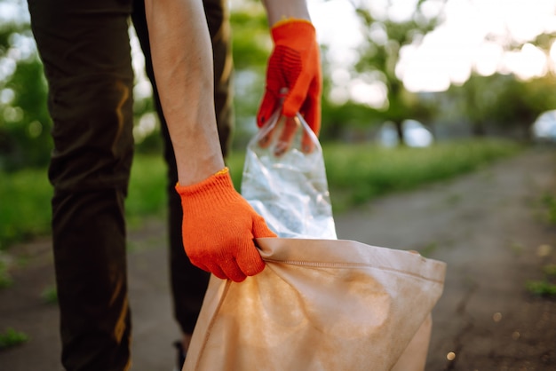 Ręka Mężczyzny Zbiera Plastikowe śmieci Do Czyszczenia W Parku. Wolontariusz W Rękawicach Ochronnych Zbiera Plastik Butelki.