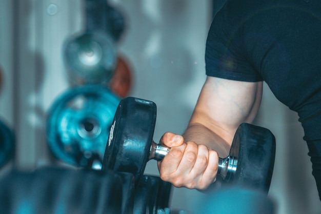 Ręka młodego przystojnego trenera fitness mięśni zamknąć się z ciężarem.